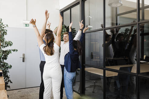 Geschäftsleute mit erhobenen Händen stehen im Kreis in einem modernen Büro - DCRF01367