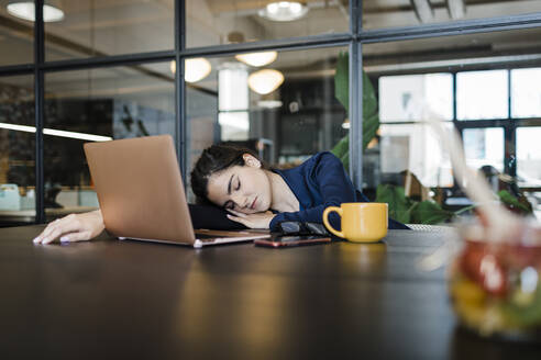 Müde Geschäftsfrau mit Laptop, die ein Nickerchen im Büro macht - DCRF01383