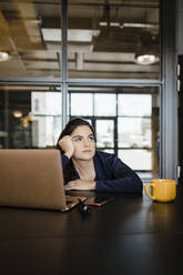 Kontemplative Geschäftsfrau, die im Büro am Laptop sitzt - DCRF01385