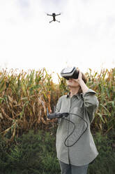 Frau mit VR-Brille und Fernbedienung bedient Drohne im Maisfeld - EKGF00087