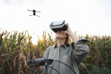 Frau mit VR-Brille und Fernbedienung bedient Drohne im Maisfeld - EKGF00088