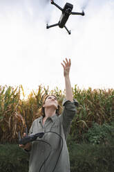 Frau mit Fernsteuerung, die eine Drohne im Maisfeld bedient - EKGF00091