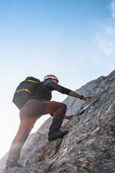 Mountaineer climbing on rocky wall under blue sky - MCVF01005