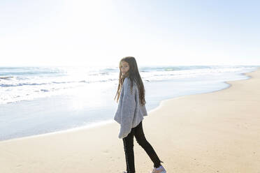 Mädchen mit Pullover steht am Strand an einem sonnigen Tag - MEGF00070