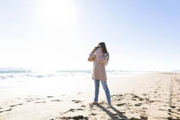 Stehendes Mädchen mit Kamera, das am Strand fotografiert - MEGF00074