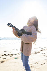 Fröhliches, Gitarre spielendes Mädchen am Strand stehend - MEGF00082