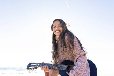 Happy girl playing guitar at beach on sunny day - MEGF00083