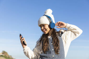 Mädchen, das ein Smartphone benutzt und mit Kopfhörern Musik hört, genießt einen sonnigen Tag - MEGF00099