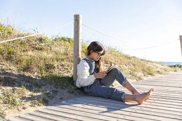 Mädchen, das ein Buch liest und sich an einen Mast an der Promenade lehnt - MEGF00109