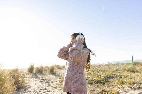 Girl wearing ear muffs at beach on sunny day - MEGF00118