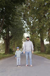 Lächelnder Mann hält die Hand seines Sohnes auf dem Fußweg - ONAF00021
