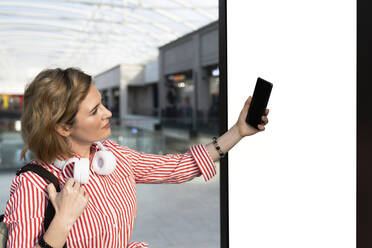 Woman taking selfie in front of billboard - EKGF00099