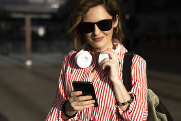 Smiling woman wearing sunglasses using smart phone - EKGF00111