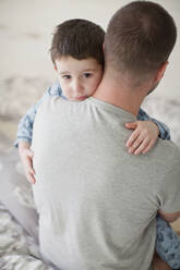 Man carrying sad boy on bed at home - ONAF00051