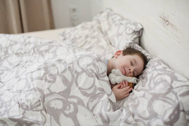 Smiling boy with toy sleeping on bed - ONAF00053