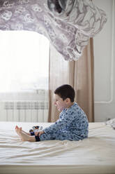 Playful boy sitting on bed under blanket in mid-air - ONAF00057