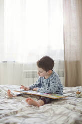 Junge liest Buch auf dem Bett - ONAF00063