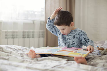 Boy reading book on bed at home - ONAF00064