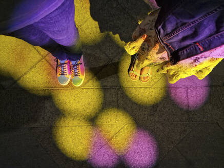 Colorful lights falling on man's shoes standing by daughter on footpath - JSMF02412