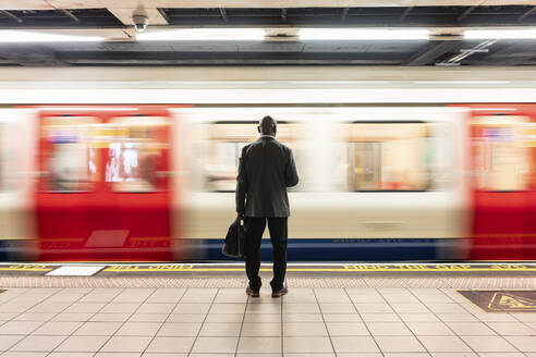 Senior businessman standing in front of speeding train on subway platform - WPEF06402