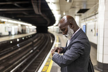 Senior businessman checking time on wristwatch waiting at subway station - WPEF06406