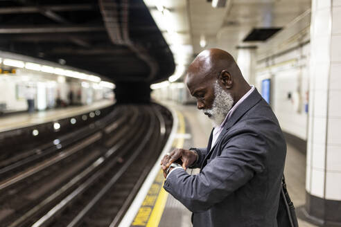 Älterer Geschäftsmann prüft die Zeit auf der Armbanduhr beim Warten in der U-Bahn-Station - WPEF06406