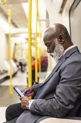 Glatzköpfiger älterer Geschäftsmann benutzt Mobiltelefon in der U-Bahn - WPEF06417