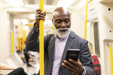 Älterer Pendler, der ein Mobiltelefon benutzt und eine Stange im Zug hält - WPEF06418