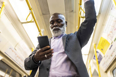 Älterer Geschäftsmann benutzt Mobiltelefon in der U-Bahn - WPEF06420