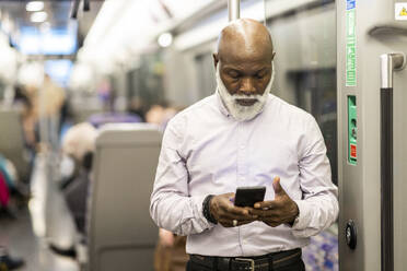 Bald senior passenger using mobile phone in train - WPEF06427