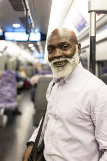 Lächelnder älterer Geschäftsmann, der im Zug reist - WPEF06428
