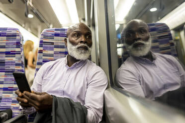 Älterer Geschäftsmann mit Smartphone schaut durch ein Fenster im Zug - WPEF06431