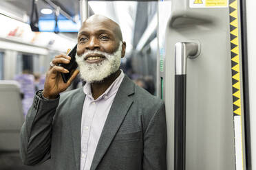 Lächelnder Geschäftsmann, der im Zug mit seinem Smartphone telefoniert - WPEF06435