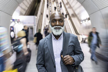Lächelnder glatzköpfiger Geschäftsmann mit Laptoptasche inmitten von Pendlern in einer U-Bahn-Station - WPEF06442