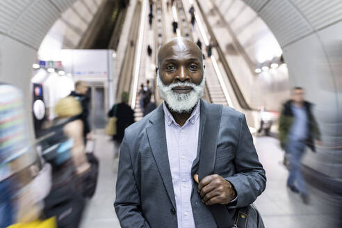 Smiling bald businessman with laptop bag amidst commuters at subway station - WPEF06442