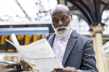 Senior businessman reading newspaper at railroad station - WPEF06457