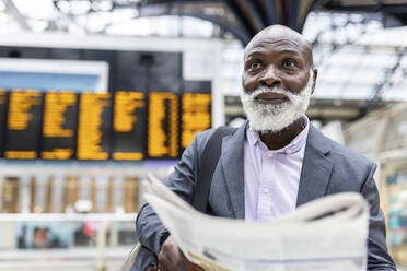 Lächelnder älterer Pendler mit Zeitung am Bahnhof - WPEF06458