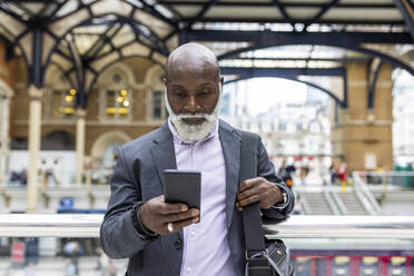 Älterer Pendler, der am Bahnhof ein Mobiltelefon benutzt - WPEF06460