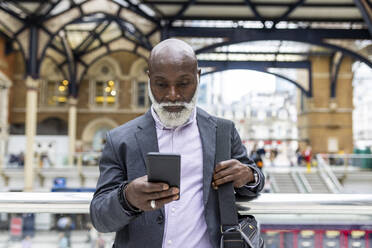 Senior commuter using mobile phone at railroad station - WPEF06460