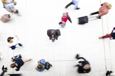 Businessman using mobile phone surrounded by commuters at railroad station - WPEF06464