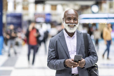 Smiling bald commuter with mobile phone at railroad station - WPEF06465