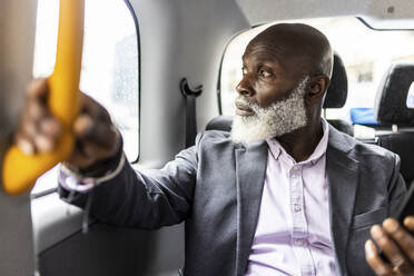 Älterer Geschäftsmann hält einen Griff und schaut durch ein Taxifenster - WPEF06481
