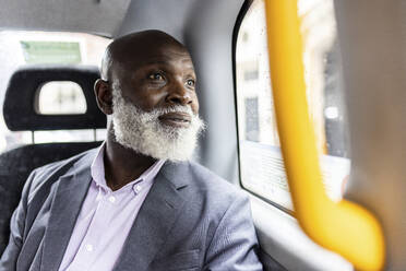 Älterer Geschäftsmann mit Bart blickt durch ein Taxifenster - WPEF06483