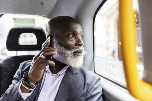 Älterer Geschäftsmann, der mit seinem Smartphone spricht und durch das Fenster im Taxi schaut - WPEF06484