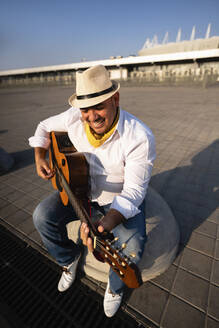 Lächelnder Straßenmusiker spielt Gitarre an einem sonnigen Tag - EKGF00126