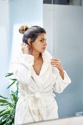 Woman wearing white bathrobe looking at mirror - VEGF05968