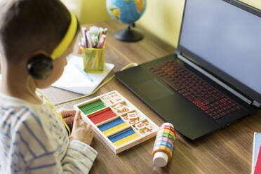 Boy wearing headphones counting sticks in front of laptop - ONAF00090