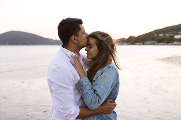 Young man kissing girlfriend's forehead at beach - EGHF00549