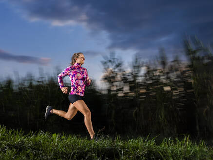 Junge Sportlerin läuft in der Abenddämmerung auf Gras - STSF03494