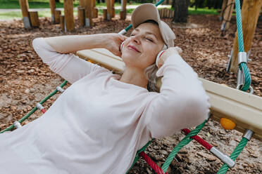 Mature woman listening to music and relaxing on hammock in park - YTF00038